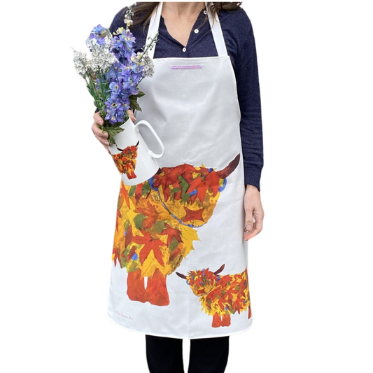 Autumn Leaf Highland Cow Apron worn by a woman with a jug of flowers in her hand on a white background.