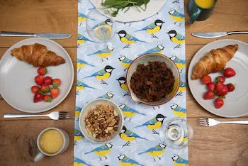 Garden Bird Table Runner on wooden table with plates of food, cutlery, mugs and glasses.  