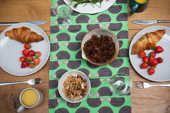 Green Hedgehog Table Runner on wooden table set with cutlery and with plates of food, mugs and glasses.