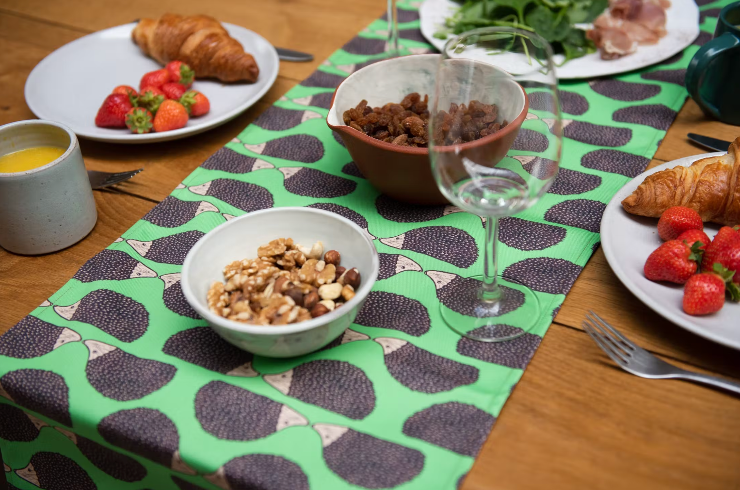 Green Hedgehog Table Runner on wooden table with plates of food, cutlery, mugs and glasses.  