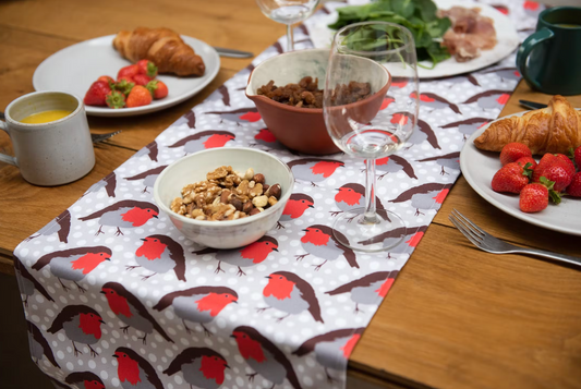 Robin Redbreast Table Runner on wooden table with cutlery, plates of food, mugs and glasses.  