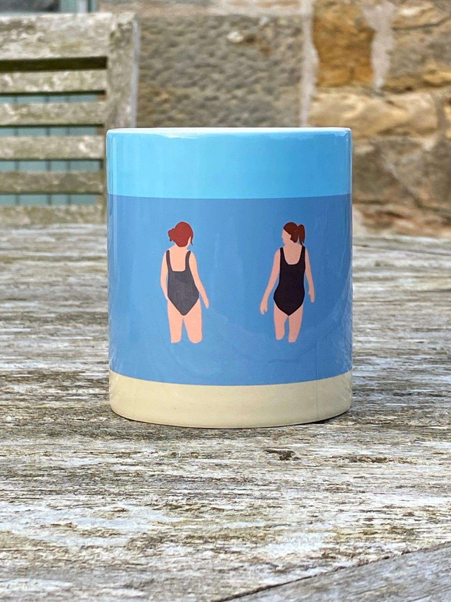 Wild Friends Wild Swimming Mug outside on wooden table with stone wall behind.